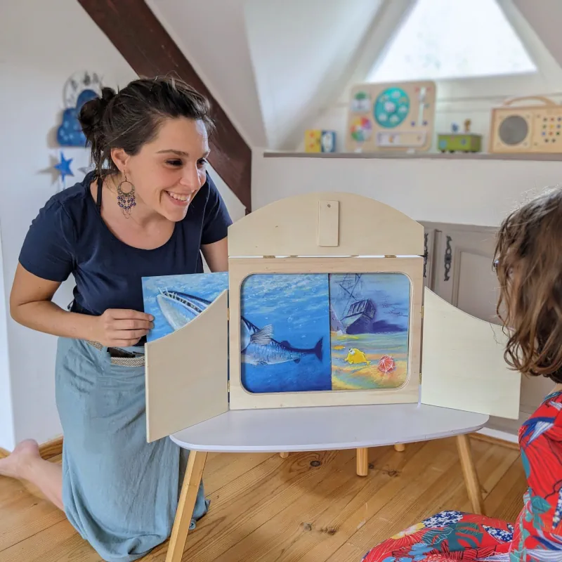 Moment de partage en famille : La fondatrice de Mon Petit Kami, Juliette Blavier, lit un kamishibaï à sa fille de 6 ans. Le butaï est en bois clair, et c'est l'histoire d'un poisson.